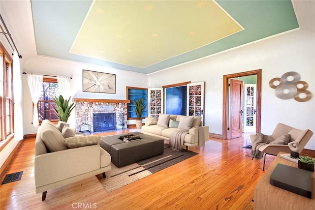 living room with a raised ceiling, a brick fireplace, and light wood-type flooring