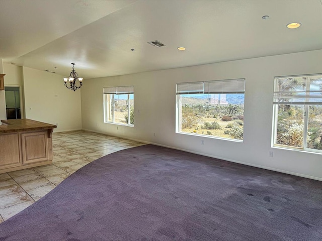 unfurnished living room featuring a chandelier, a healthy amount of sunlight, and light carpet