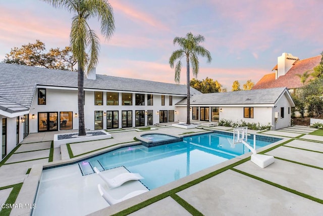 pool at dusk featuring a patio area and an in ground hot tub