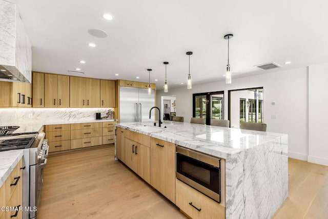 kitchen featuring built in appliances, light hardwood / wood-style flooring, a large island, and sink