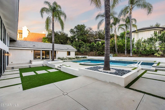 pool at dusk with an in ground hot tub and a patio