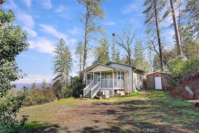 view of front of property featuring covered porch, a front yard, and a storage shed