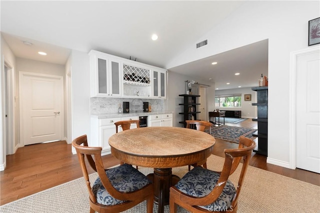 dining space with lofted ceiling, dark wood-type flooring, and bar area