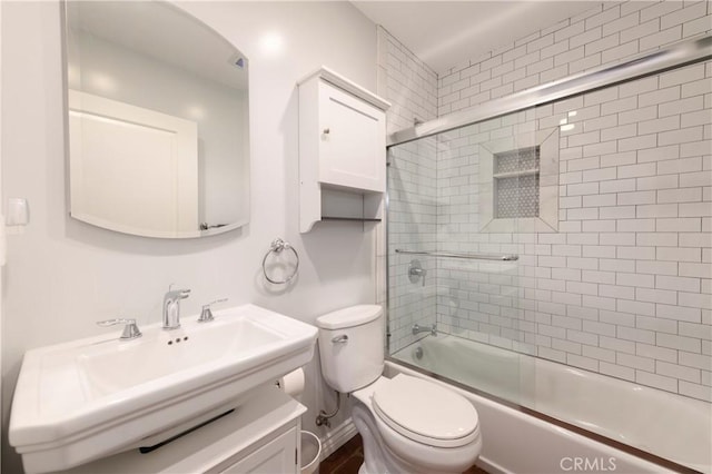 full bathroom featuring sink, bath / shower combo with glass door, and toilet