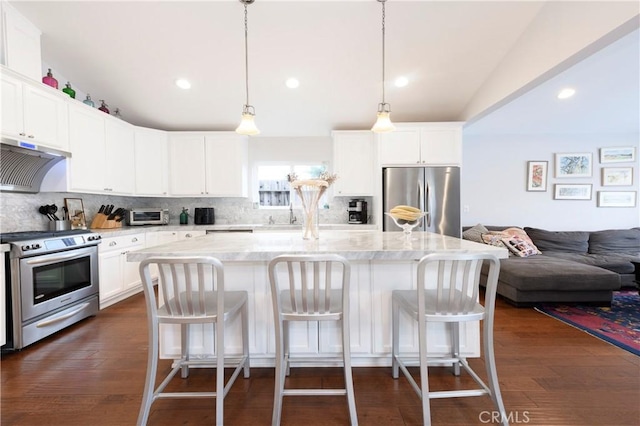 kitchen with light stone countertops, a center island, stainless steel appliances, decorative light fixtures, and exhaust hood