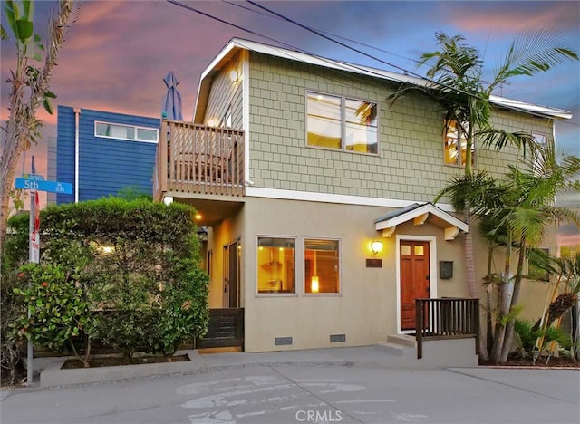 view of front of home with stucco siding, a balcony, and crawl space