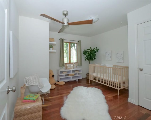 bedroom with a ceiling fan, a nursery area, and wood finished floors