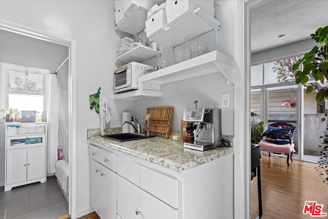 kitchen with a textured ceiling, white cabinetry, sink, and a wealth of natural light