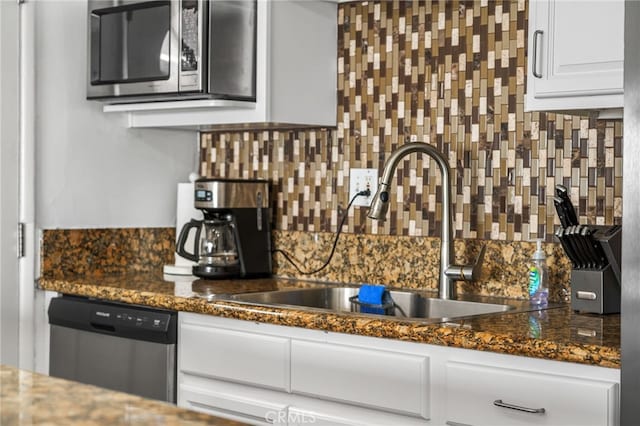 kitchen with appliances with stainless steel finishes, backsplash, sink, dark stone countertops, and white cabinets