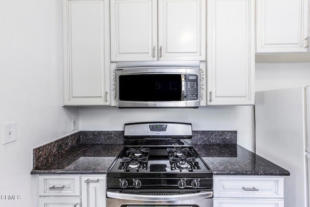 kitchen featuring white cabinets, stainless steel appliances, and dark stone counters