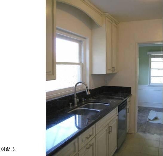 kitchen featuring dark stone counters, sink, cream cabinets, dishwasher, and light tile patterned flooring