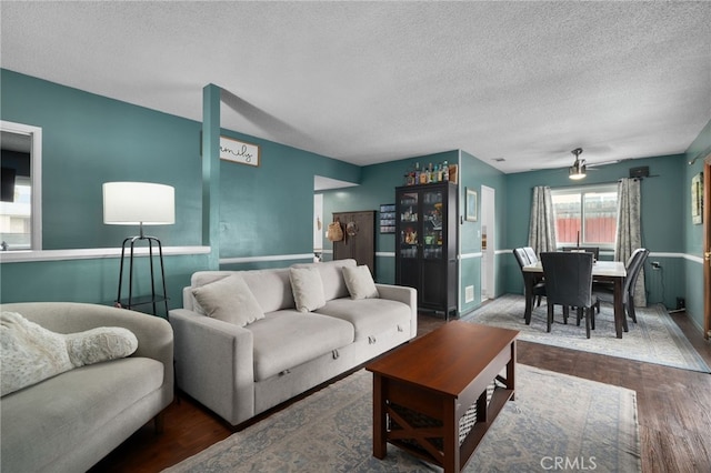 living room with a textured ceiling, ceiling fan, and dark wood-type flooring