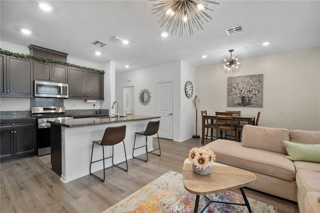 kitchen featuring an inviting chandelier, light hardwood / wood-style flooring, an island with sink, appliances with stainless steel finishes, and a breakfast bar area