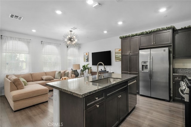 kitchen featuring sink, light wood-type flooring, an island with sink, stainless steel appliances, and a chandelier