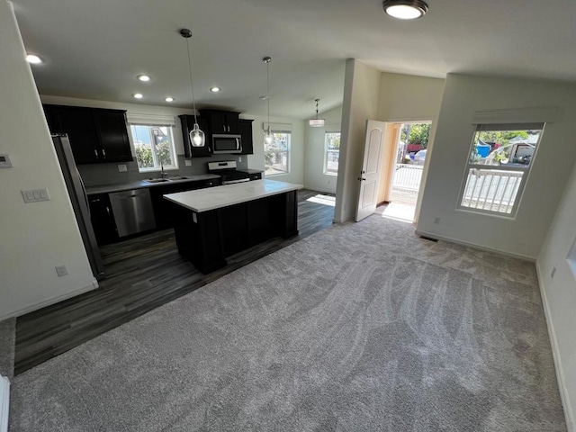 kitchen with dark carpet, vaulted ceiling, appliances with stainless steel finishes, decorative light fixtures, and a kitchen island