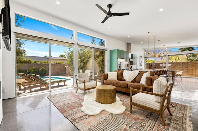 living room featuring concrete floors, a healthy amount of sunlight, and ceiling fan with notable chandelier