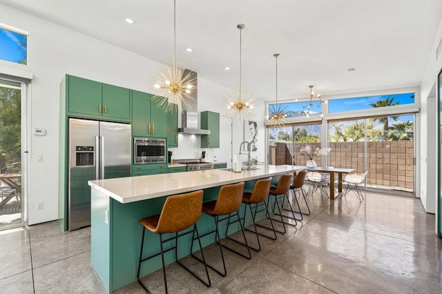 kitchen with appliances with stainless steel finishes, wall chimney range hood, green cabinetry, a chandelier, and a breakfast bar area