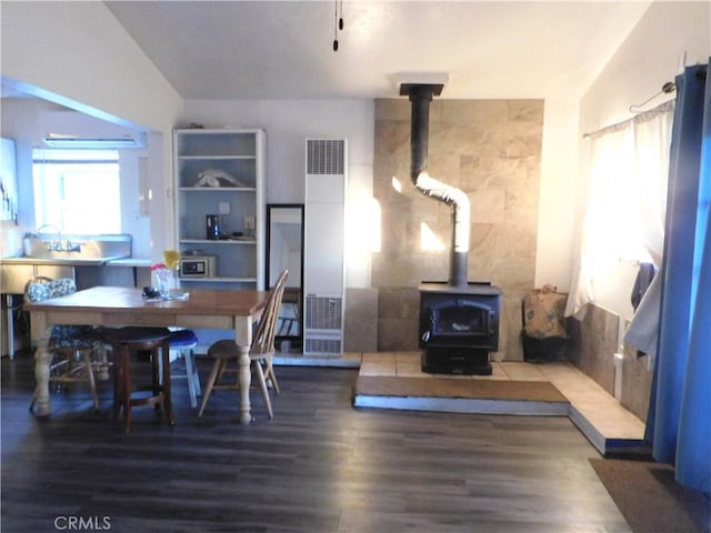 dining space with vaulted ceiling, a wood stove, and wood-type flooring