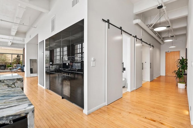 corridor with a barn door, light hardwood / wood-style flooring, and a high ceiling