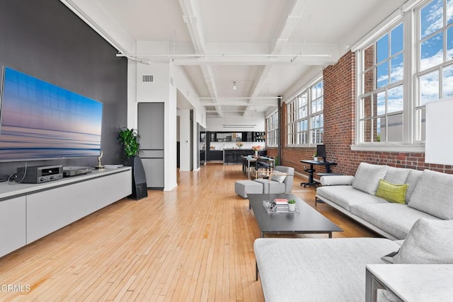 living room featuring beam ceiling, light hardwood / wood-style flooring, and brick wall