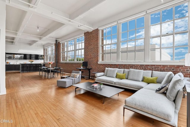 living room with beamed ceiling, light hardwood / wood-style floors, sink, and brick wall