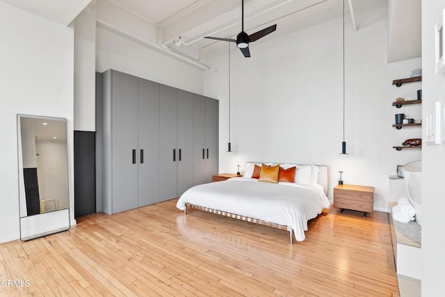 bedroom with ceiling fan, a towering ceiling, and light wood-type flooring