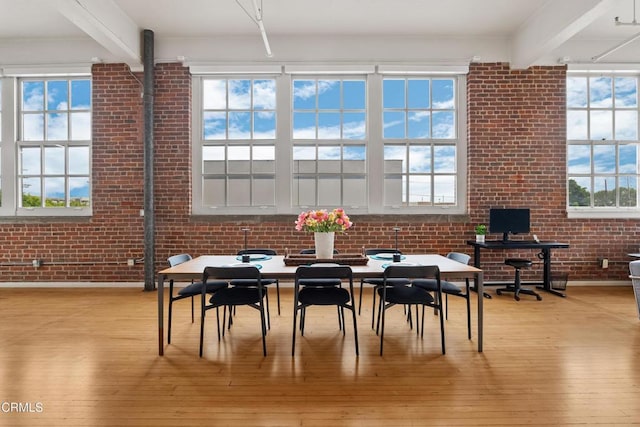 dining space with beam ceiling, brick wall, and light wood-type flooring