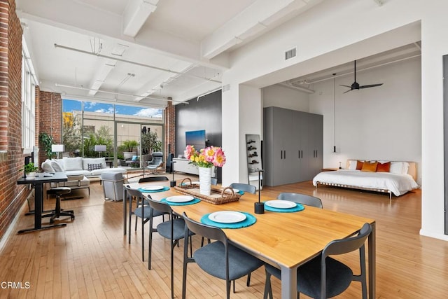 dining area featuring beam ceiling, ceiling fan, light hardwood / wood-style flooring, and brick wall