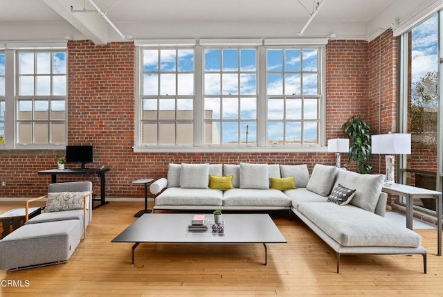 living room with a wealth of natural light, brick wall, and light hardwood / wood-style flooring