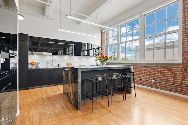 kitchen featuring a center island, sink, light hardwood / wood-style flooring, brick wall, and a breakfast bar area