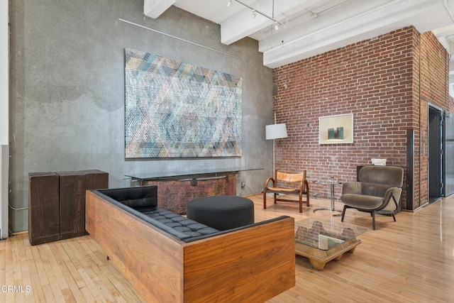 interior space with track lighting, light hardwood / wood-style flooring, a towering ceiling, beamed ceiling, and brick wall