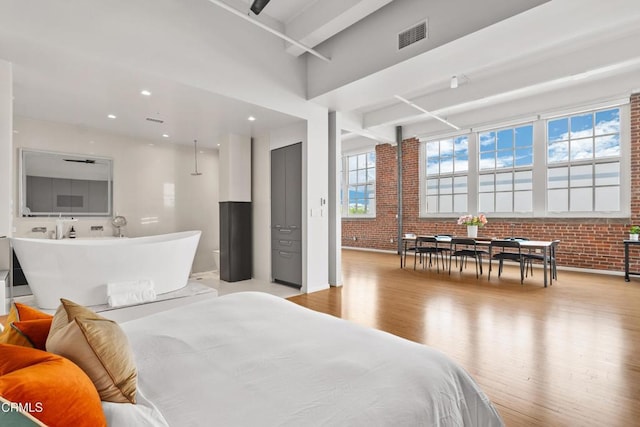 bedroom featuring multiple windows, light hardwood / wood-style flooring, and brick wall