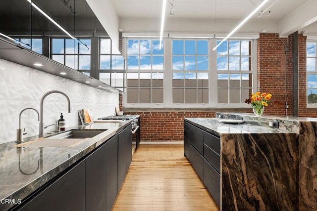 kitchen featuring light stone counters, brick wall, a healthy amount of sunlight, sink, and light hardwood / wood-style floors