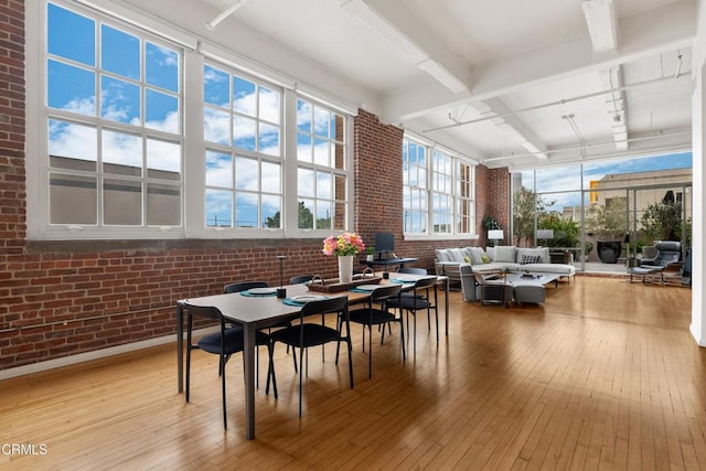 dining space with hardwood / wood-style floors, beam ceiling, and brick wall