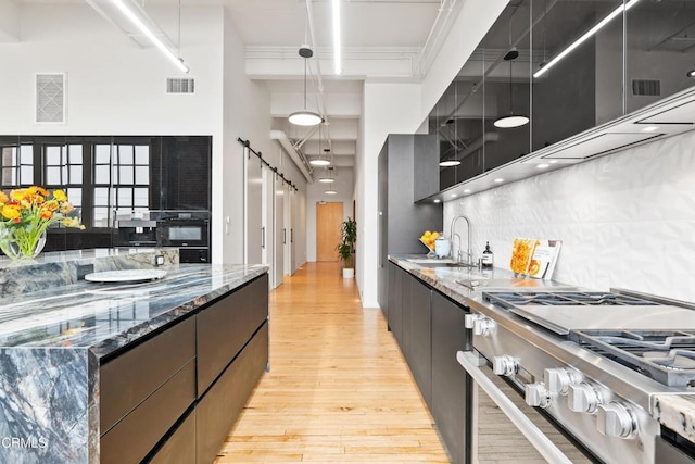 kitchen featuring high end range, a high ceiling, sink, decorative light fixtures, and light hardwood / wood-style floors