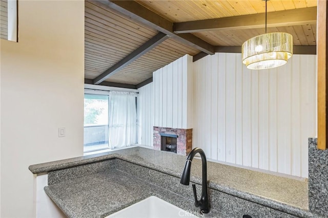 kitchen with vaulted ceiling with beams, wood walls, sink, and a fireplace