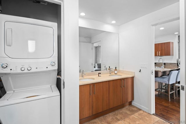 clothes washing area with stacked washer and dryer, light hardwood / wood-style flooring, and sink