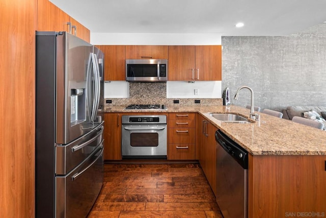 kitchen with sink, dark wood-type flooring, light stone counters, kitchen peninsula, and appliances with stainless steel finishes