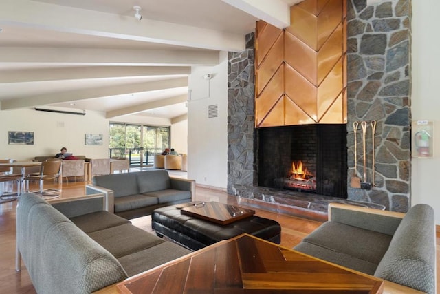 living room featuring beam ceiling, a stone fireplace, and wood-type flooring