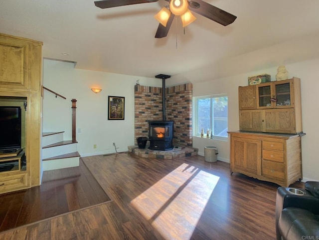 living room with ceiling fan, a wood stove, and dark wood-type flooring