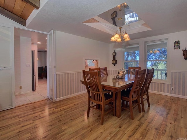 dining space with a textured ceiling, a chandelier, vaulted ceiling, and light wood-type flooring