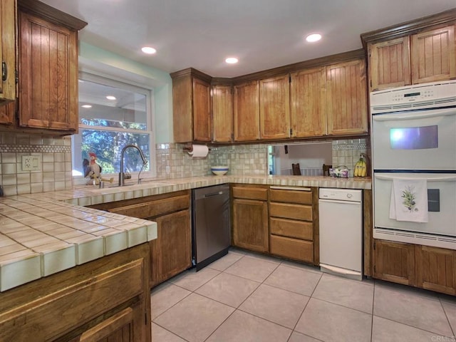 kitchen featuring dishwasher, sink, double oven, tasteful backsplash, and tile counters