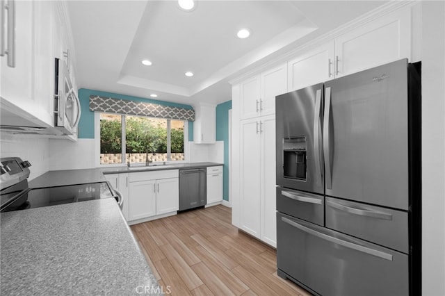 kitchen with backsplash, stainless steel appliances, a tray ceiling, light hardwood / wood-style flooring, and white cabinets