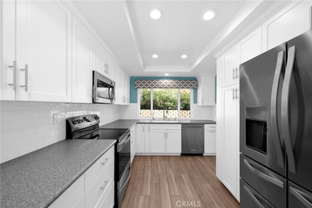 kitchen featuring appliances with stainless steel finishes, light wood-type flooring, a raised ceiling, sink, and white cabinets