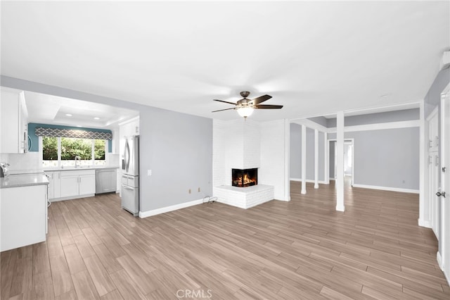 unfurnished living room featuring ceiling fan, light hardwood / wood-style floors, sink, and a brick fireplace