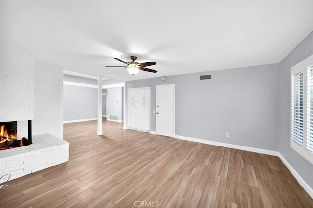 unfurnished living room with a brick fireplace, light hardwood / wood-style flooring, and ceiling fan