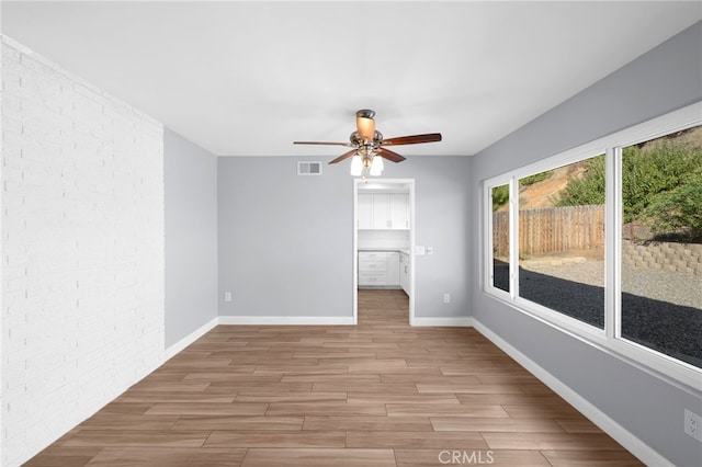 unfurnished room with ceiling fan, light wood-type flooring, and brick wall