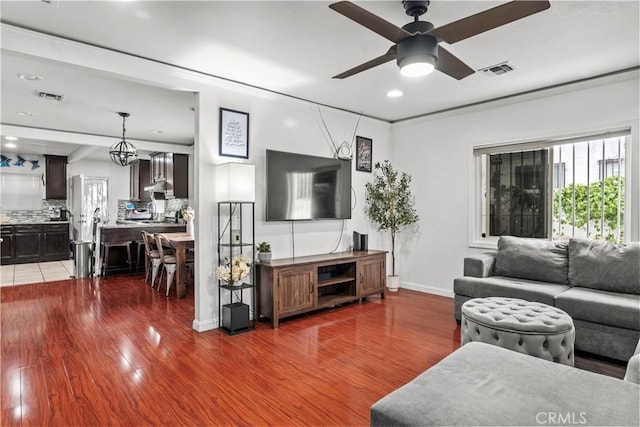 living room with ornamental molding, ceiling fan with notable chandelier, and hardwood / wood-style flooring