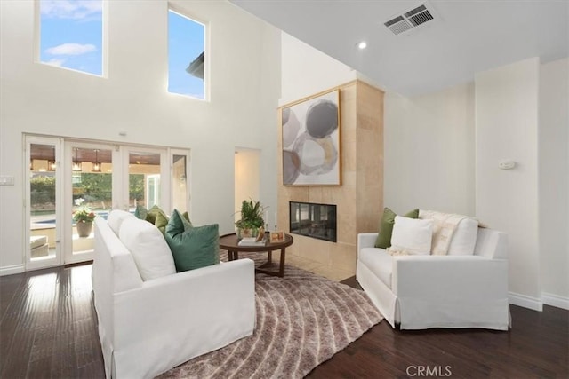 living room with a high ceiling, dark wood-type flooring, and a tiled fireplace