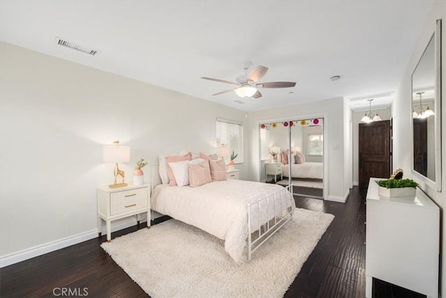 bedroom with ceiling fan with notable chandelier and dark wood-type flooring